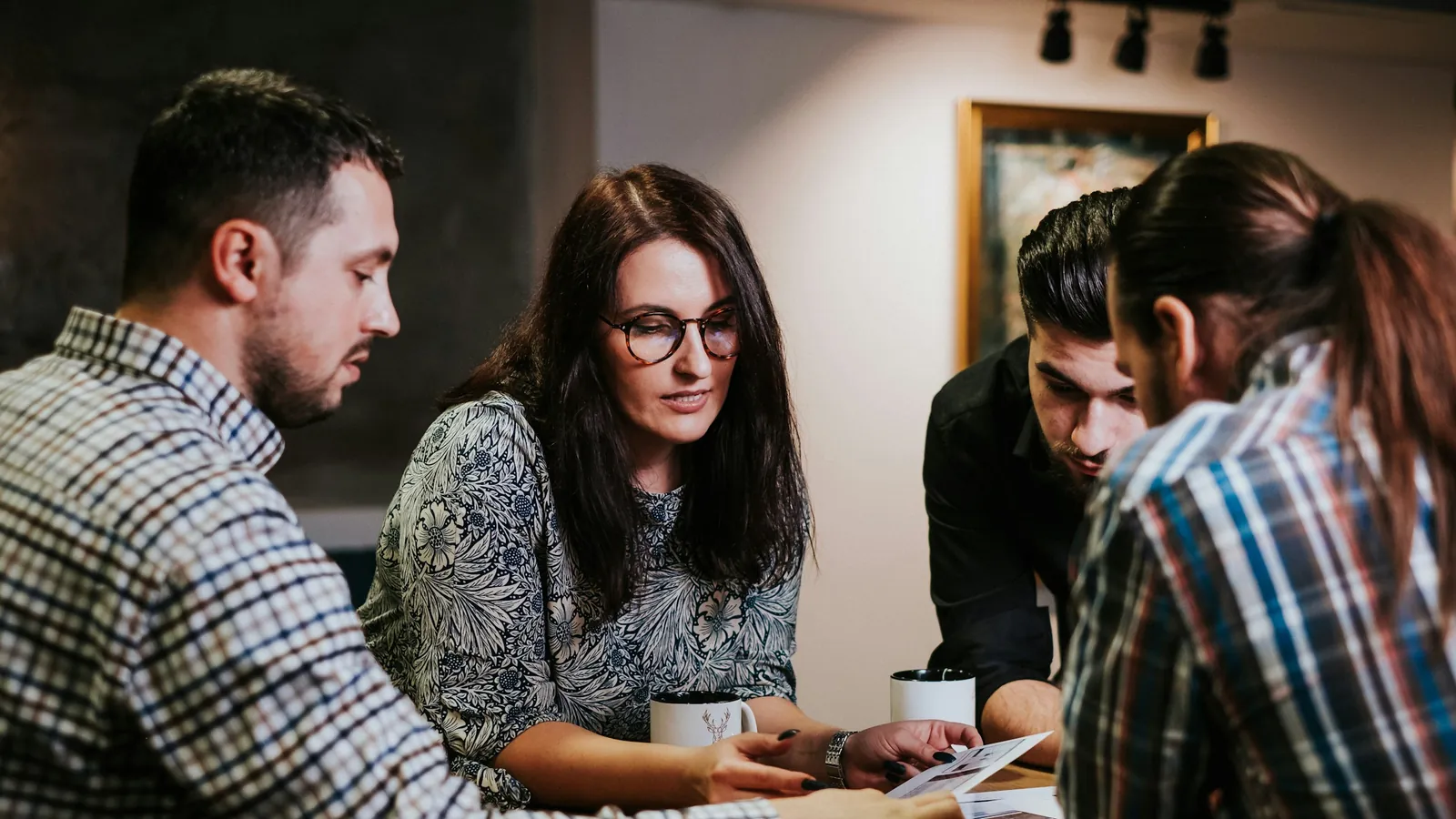 Four colleagues lean over a wooden table, reviewing printed pages together