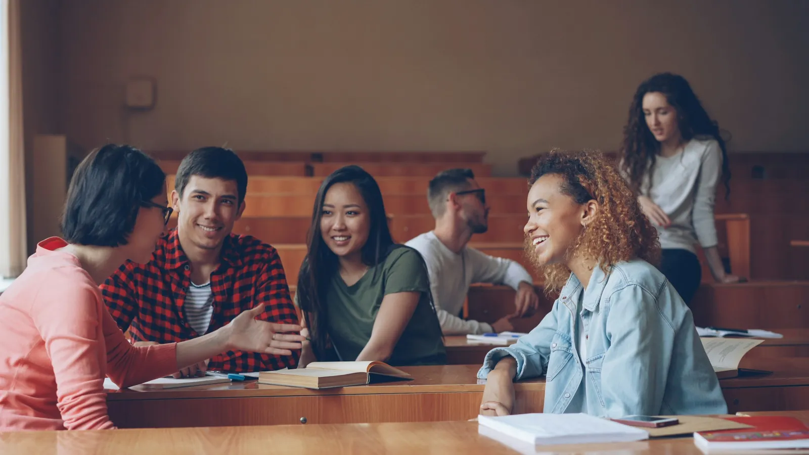 University students talk and laugh together at their desks in a lecture hall